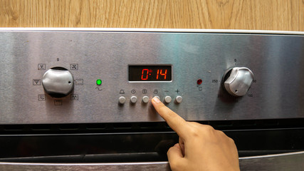 Close up view of girl hand setting up the timer delay for baking at the kitchen