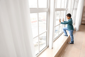 Little African-American boy near window. Child in danger