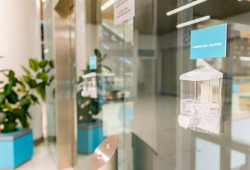 Sanitizer box with detergent liquid sticked to the glass next to elevator in shopping mall. Cleanlines and safety during pandemic of Corona virus. 2020