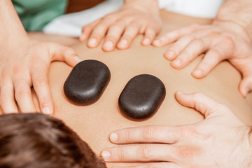 Hands of massage therapists doing back massage while hot stones on back of man closeup in spa.