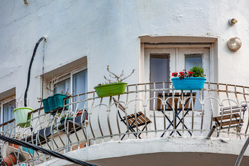 Balcony of round old-fashioned building, brown wooden table with two chairs, wrought iron fence with flower pots fixed on it, outdoor view, Tel-Aviv city