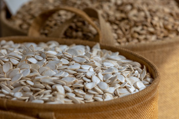 Pile of white pumpkin seeds in brown wooden bowl at food marketplace, blurred seeds on foreground