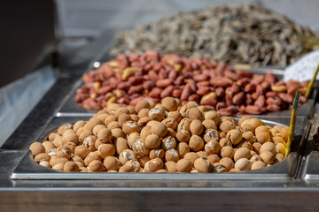 Variety of nuts in tray at food market on sunlight, macadamia nuts in focus on foreground, blurred pistachio on foreground 