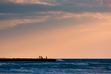 Four people group silhouette standing on pier all together near to stormy deep blue sea, orange sunset sky