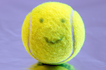 green tennis ball covered with felt and with a smiling face on a purple background