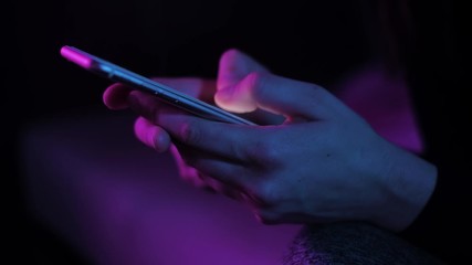 Young woman texting chatting on smart phone at night; girls finger tapping keypad, writing message on mobile devices touchscreen, blue low light; close up top side view - Powered by Adobe