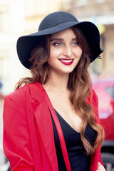 Portrait of smiling young woman in black hat looking at camera outdoors.