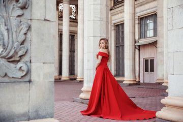 Beautiful blonde girl in a red long dress on a background of architecture, columns 