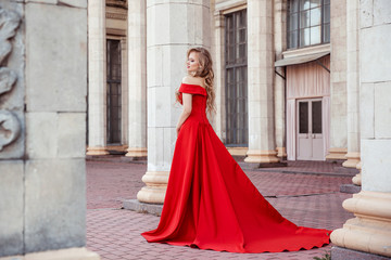 Beautiful blonde girl in a red long dress on a background of architecture, columns 