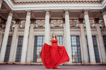 Beautiful blonde girl in a red long dress on a background of architecture, columns 