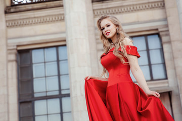 Beautiful blonde girl in a red long dress on a background of architecture, columns 