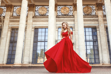 Beautiful blonde girl in a red long dress on a background of architecture, columns 