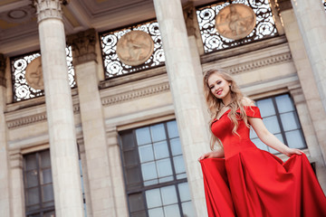 Beautiful blonde girl in a red long dress on a background of architecture, columns 