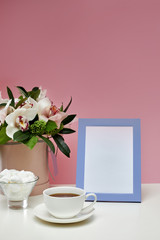 photo frame, orchid flowers, cup of tea and sweets on the pink background. empty space for text. mock up with copy space.