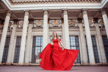 Beautiful blonde girl in a red long dress on a background of architecture, columns 