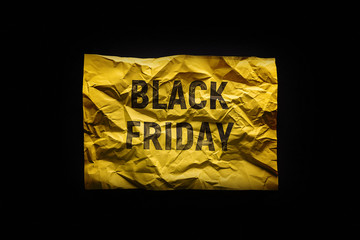 The phrase black Friday on crumpled yellow paper. Invitation to the sale. Black background.