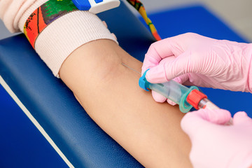 Nurse takes blood sampling introducing a needle into a vein of woman's arm.
