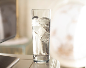 Glasses of water with pieces of ice on a nightstand illuminated by the sun