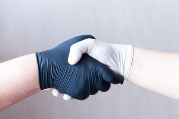 Handshake in protective medical gloves in black and white colors, close up