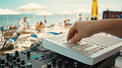 DJ hand and mixer close-up. Summer music party on the beach. On a blurred background people and the sea