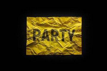 The word party on crumpled yellow paper. Invitation to the celebration. Black background.