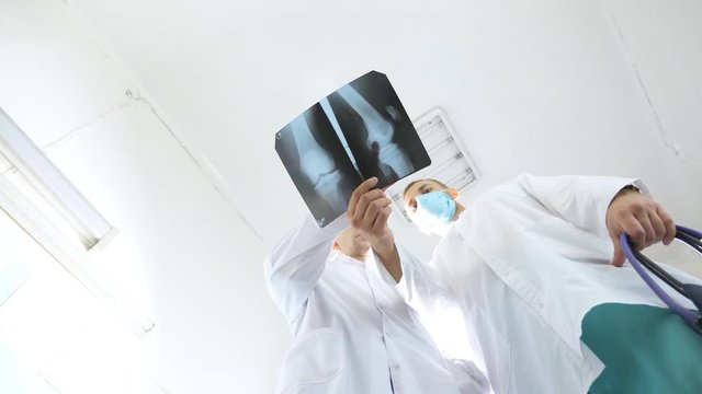 Medical workers in hospital examine x-ray prints. Male medics consult with each other while looking at x ray image. Two caucasian doctors view mri picture and discussing about it. Low angle of view