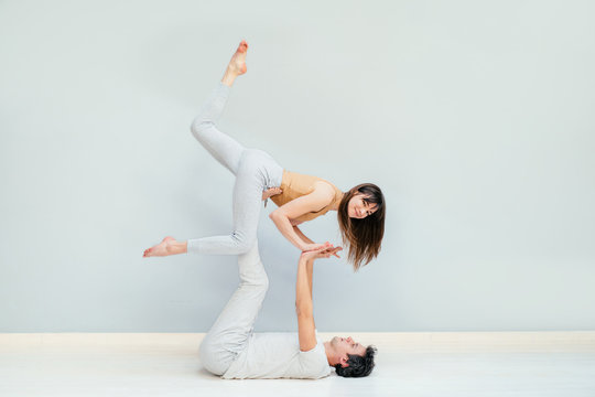 Loving young couple having acro yoga practice in bed at home, sporty strong shirtless man holding slender attractive woman, happy smiling girlfriend doing sport exercise with boyfriend, trust concept