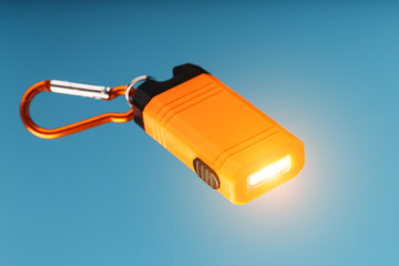 An orange led flashlight with a carabiner glows on a blue background.