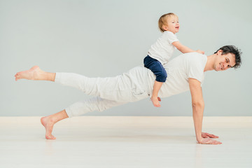 Fototapeta na wymiar Positive sportive father doing pilates, yoga exercise, workout at home in floor with his little baby son having fun, excited emotion, play together, communication concept.