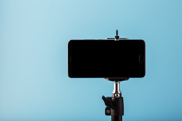 Mobile phone on a tripod with a clear black display for image and text, blue isolated background.