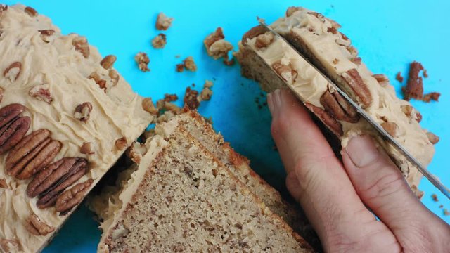 A 4K shot of a homemade cake. An over the top view of pecans on top of a banana cake covered with butter cream. Woman cutting/slicing a cake with a knife. Cutting the birthday cake.