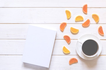 white cup of coffee, white paper and multicolored fruit marmalade lie on a white wooden background