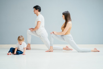Obraz premium young sporty mother does physical yoga or pilates exercises together with her baby son over gray background. Fitness, happy maternity and healthy lifestyle concept.