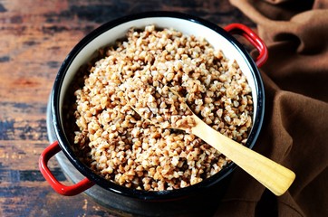 Boiled buckwheat with butter in a pan on a dark wooden background
