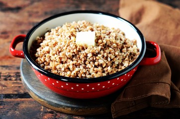 Boiled buckwheat with butter in a pan on a dark wooden background