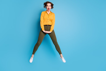 Fototapeta na wymiar Full length photo of pretty business lady jumping high up open mouth not believe boss promoted her wear yellow shirt green pants footwear isolated bright blue color background