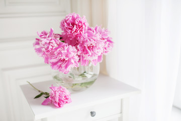 Pink peonies in glass vase. Flowers on a white table near the window. Beautiful peony flower for catalog or online store. Floral shop and delivery concept. Banner. Copy space