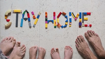 The concept of self-isolation during quarantine from coronavirus. Toy blocks are laid out to encourage you to stay at home, and next to the feet of all family members: mom, dad, son and daughter - Powered by Adobe