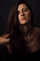 Vogue style close-up fashion portrait of beautiful young woman with long dark hair on black background.