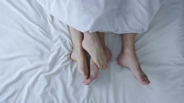 Male and female legs in bed. Couple in bed making petting and love. Romantic couple relaxing together touching legs. Top view. Marriage, family, love, sex concept.