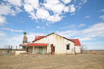 old abandoned derelict house in the desert sand with blue skies.