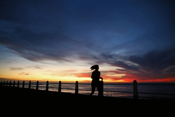 Silhouetted sportswoman training for fitness on seaside promenade at sunset running. © Brett