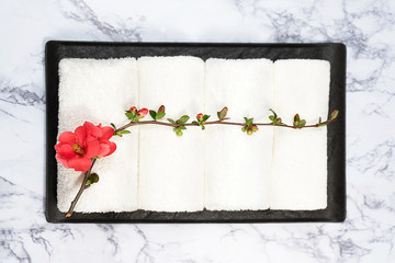 Beauty and spa concept. White towels and red flower on black tray on marble background.