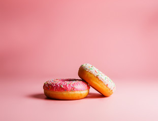 Two juicy fresh sweet donuts with sugar icing and sprinkles on a pink background