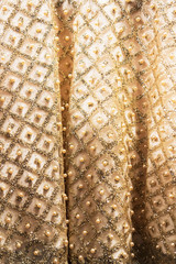 Wedding dress fabric texture background. Golden and ivory silk dress with beads, pearls, sparkles and embroidery. Vintage wedding dress detail. Elegant geometric pattern on fabric. Vertical, close up