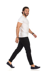 Handsome Casual Man Is Walking, Looking At Camera And Smiling. Side View.