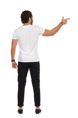 Handsome Man Is In Black Trousers And White Jeans Is Looking Away And Pointing At The Side. Rear View.
