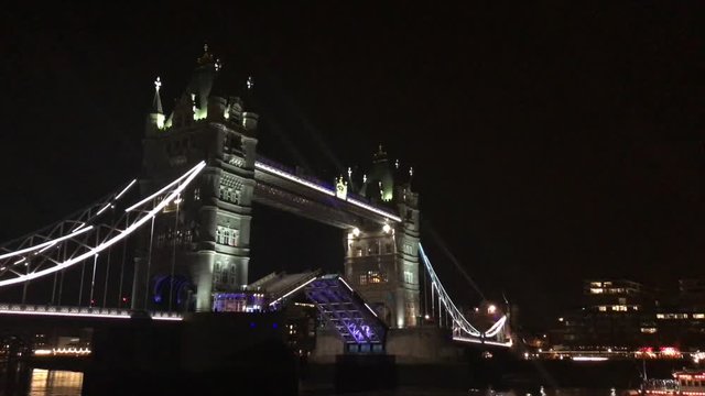 Tower Bridge of London drawbridge opening with Boat going under it at night lit up.