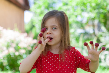 Young girl is holding raspberries on her fingers, outdoor shoot