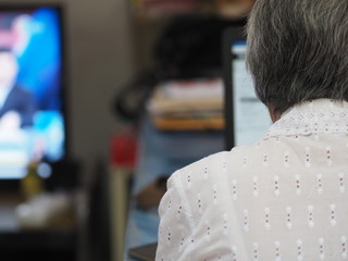 Work at home taken on the rear old woman sitting working on notebook, laptop view back